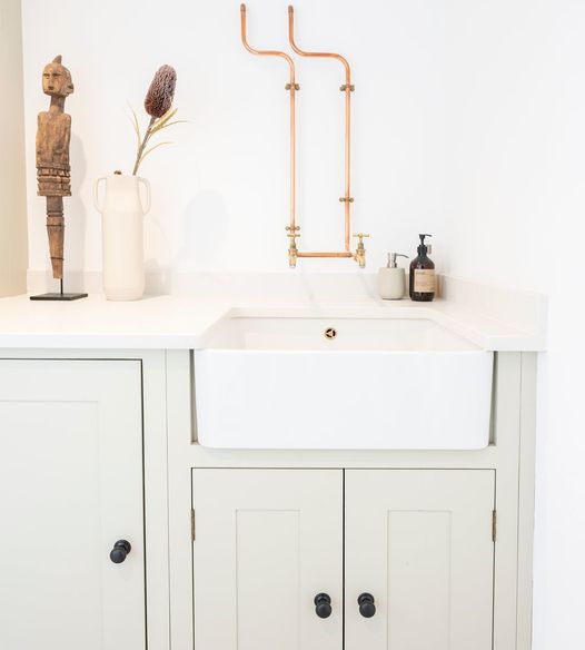 Country Kitchen image by From the Anvil showing exposed pipes, aged bronze cabinet knobs, a butlers sink, and neutral cabinets.