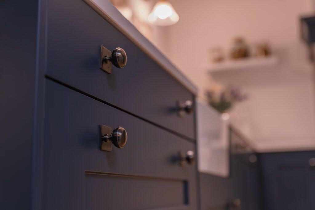 The Alexander & Wilks Quantock knob on square backplate in Black PVD shown on Blue shaker style cabinets in a marble and golden accented kitchen